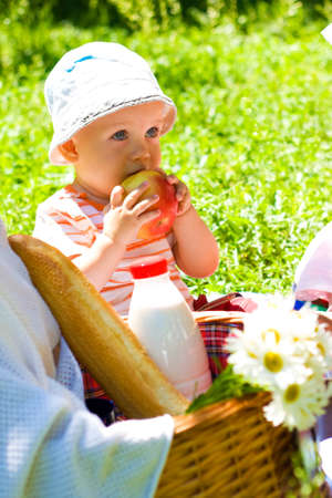 Portrait of beautiful baby boy eating apple on the lawnの写真素材