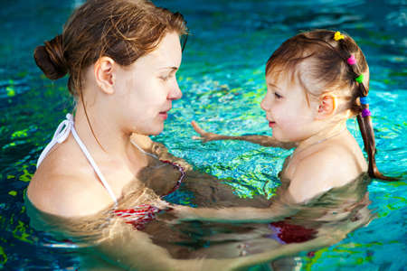 Young mother and her cute little daughter swimming in the poolの写真素材