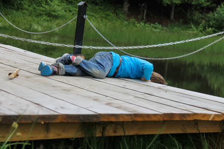 Boy lies on wooden bridge by the lakeの写真素材
