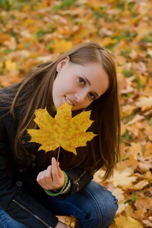 young girl holding autumn leaf at the parkの写真素材
