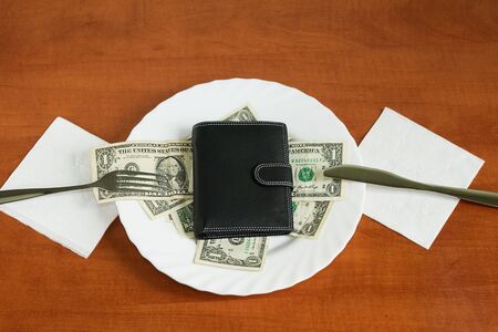 dollars and wallet on a plate with knife and fork over wooden backgroundの写真素材