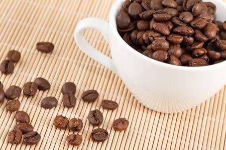 white cup full of coffee beans over bamboo backgroundの写真素材