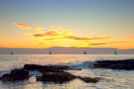 Rocky coast seascape with sailing boats at sunset の写真素材