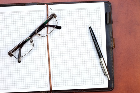 Office table with notebook, pen and glassesの写真素材