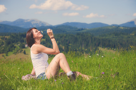 Beautiful girl smiling and lying on field of green grass and holding flowers in her handの写真素材