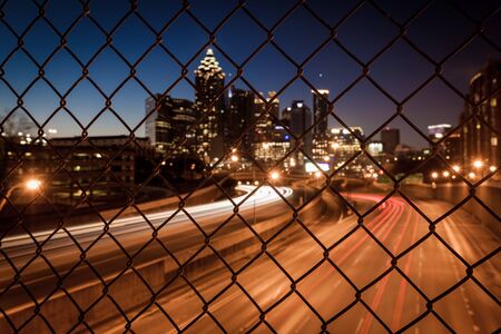 Night city skyline through the wire mesh fence. Abstract blurred cityscape backgroundの写真素材