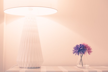 Beautiful flowers with table lamp over white wall backgroundの写真素材