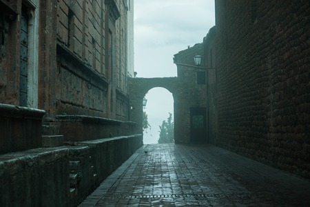 Old European narrow empty street of a medieval town at a foggy evening. Pienza, Italyの写真素材