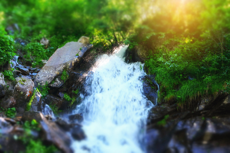 Beautiful mountain rainforest waterfall with fast flowing water and rocks, long exposure. Natural seasonal travel outdoor background with sun shihingの写真素材