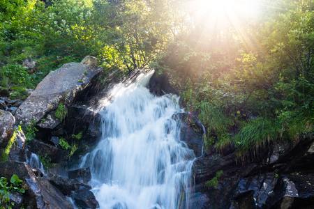 Beautiful mountain rainforest waterfall with fast flowing water and rocks, long exposure. Natural seasonal travel outdoor background with sun shihingの写真素材