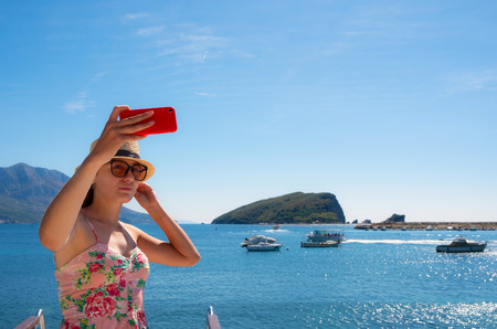 Young beautiful brunette girl in hat making selfie using phone while standing on the luxury yachtの写真素材