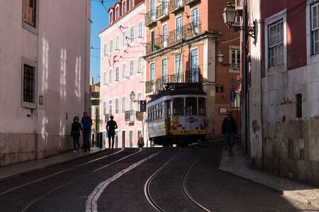 Lisbon, Portugal - March 23, 2019: Yellow tram, symbol of Lisbon at sunny street with walking...