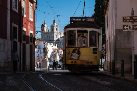 Lisbon, Portugal - March 23, 2019: Yellow tram, symbol of Lisbon at sunny street with walking touristsの写真素材
