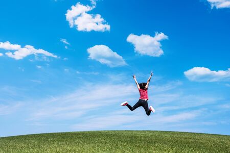 pretty young woman jumping on green grass lawn over blue sky