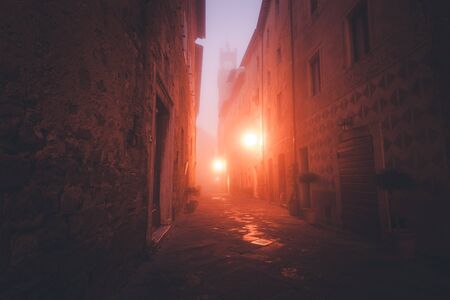 Old European narrow empty street of a medieval town at a foggy evening. Pienza, Italyの写真素材
