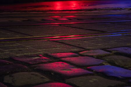 Wet illuminated by red light cobblestone street at nightの写真素材