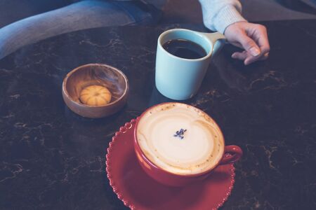 Red cup of hot cappuccino in female hand on wooden tableの写真素材