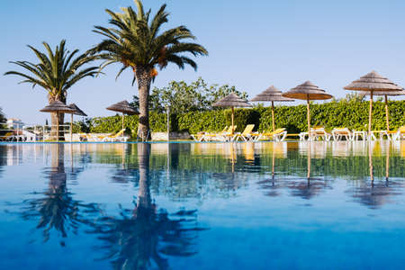 Beautiful tropical beach front hotel resort with swimming pool, sun-loungers and palm trees during a warm sunny day, paradise destination for vacationsのeditorial素材