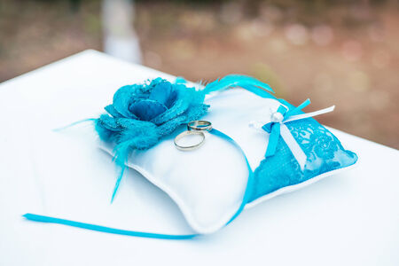gold wedding rings on the pincushion with blue flowersの写真素材
