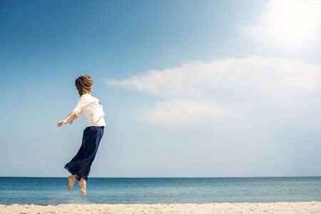 Happy young woman jumping on the beachの写真素材
