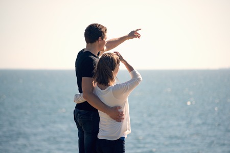 Young couple standing on a beach and looking to blue skyの写真素材