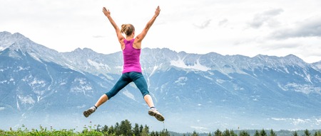 young woman jumping on top of the mountainの写真素材