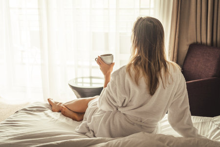 Woman in white bathrobe lying on sofa and relaxing with cup of tea at home.の写真素材
