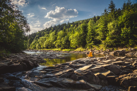 Woman doing yoga on the stone at the mountain river. Carpathiansの写真素材