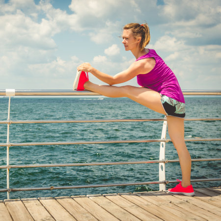 Sporty young woman stretching leg on pier at seaside in morning