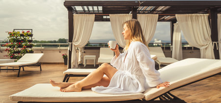 Woman in white bathrobe lying on sofa and relaxing with orange cocktail at the roof.の写真素材
