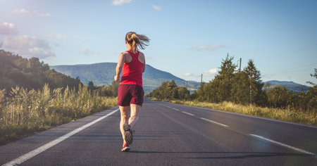 Fitness blonde woman running on the asphalt road at the mountains