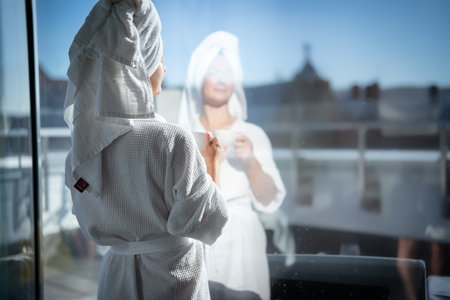 Rear view of young woman in bathrobe looking out the windowの写真素材