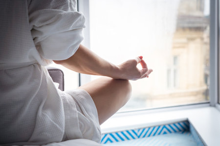 Woman in bathrobe sitting on the windowsill and meditating. Concept of relaxationの写真素材