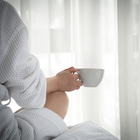 Woman in white bathrobe lying on sofa and relaxing with cup of tea at home.の写真素材