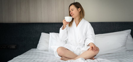 Woman in white bathrobe relaxing with cup of tea at home.の写真素材