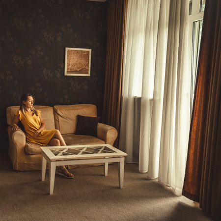 Young woman in yellow dress sitting on sofaの写真素材