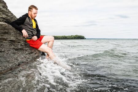 Young man sitting on a rocky cliff at a beach.の写真素材