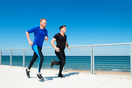 Two men running or jogging at a beachside park.の写真素材