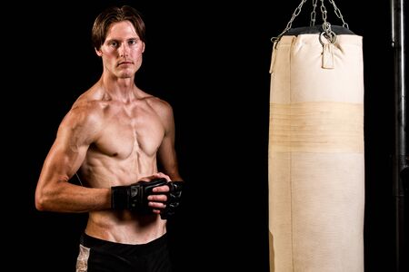 Young adult martial artist with heavy bag. Studio shot over black.の写真素材