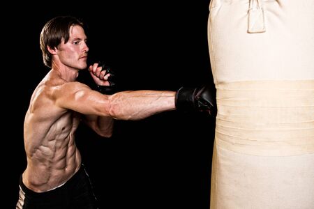 Young adult martial artist with heavy bag. Studio shot over black.の写真素材