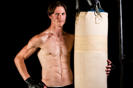 Young adult martial artist with heavy bag. Studio shot over black.の写真素材
