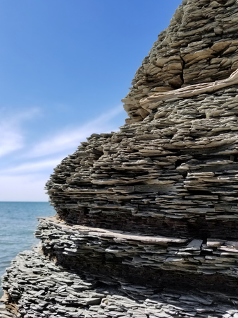 Shale cliff side at a lake shore under blue skies.
