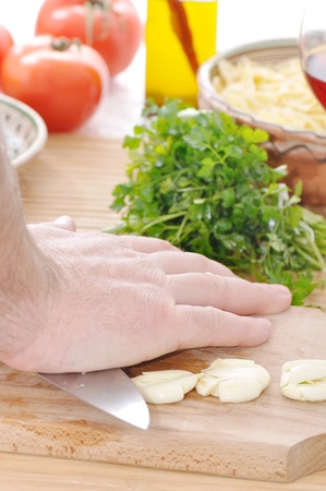 hand squashing garlic with a knife on a table with vegetable on backgroundの写真素材