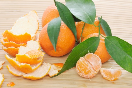peeled and fresh tangerines with green leaves on bamboo wooden plateの写真素材