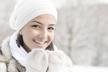 Head portrait of beautiful young woman smiling, holding cup of hot drink outside in winter. high keyの写真素材