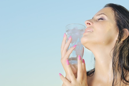 Head portrait of beautiful hot young woman holding glass with ice on her face. with copy space on blue skyの写真素材