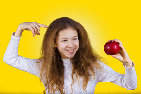 Happy, smiling little girl holding an red apple, pointing with finger to her head isolated on yellow background.Healthy food,Healthy Thinking,Positive thinking.Idea.の写真素材