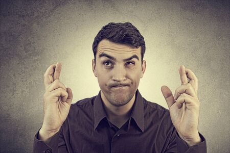 Portrait of Young man,student wishing something hardly,very much with crossed fingers over grey background.Praying for something very hardly,very much.の写真素材