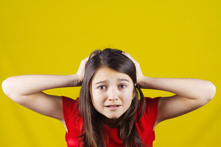 Stressed,depressed,unhappy little girl holding hands on her head over yellow background.の写真素材