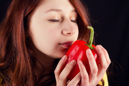 Young woman holding and smelling a fresh red pepper over black background.の写真素材